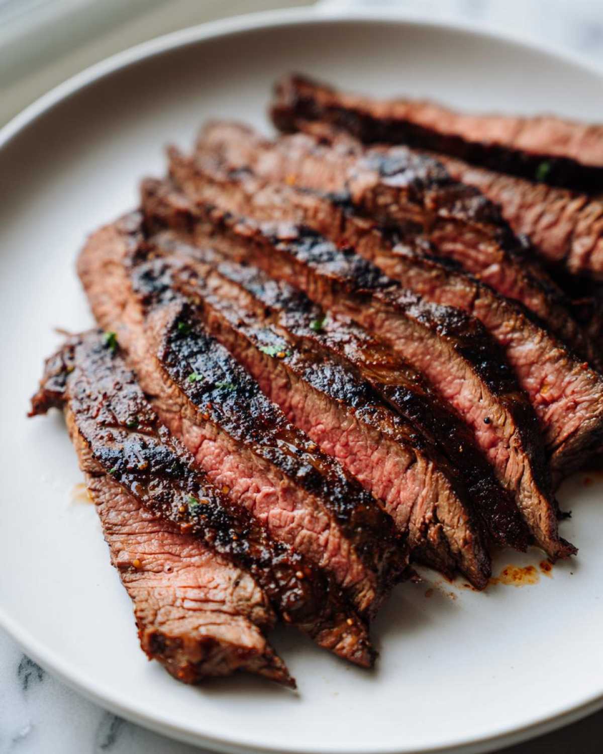 Close-up of perfectly grilled and sliced carne asada steak showing a medium-rare interior, seasoned from the carne asada marinade.