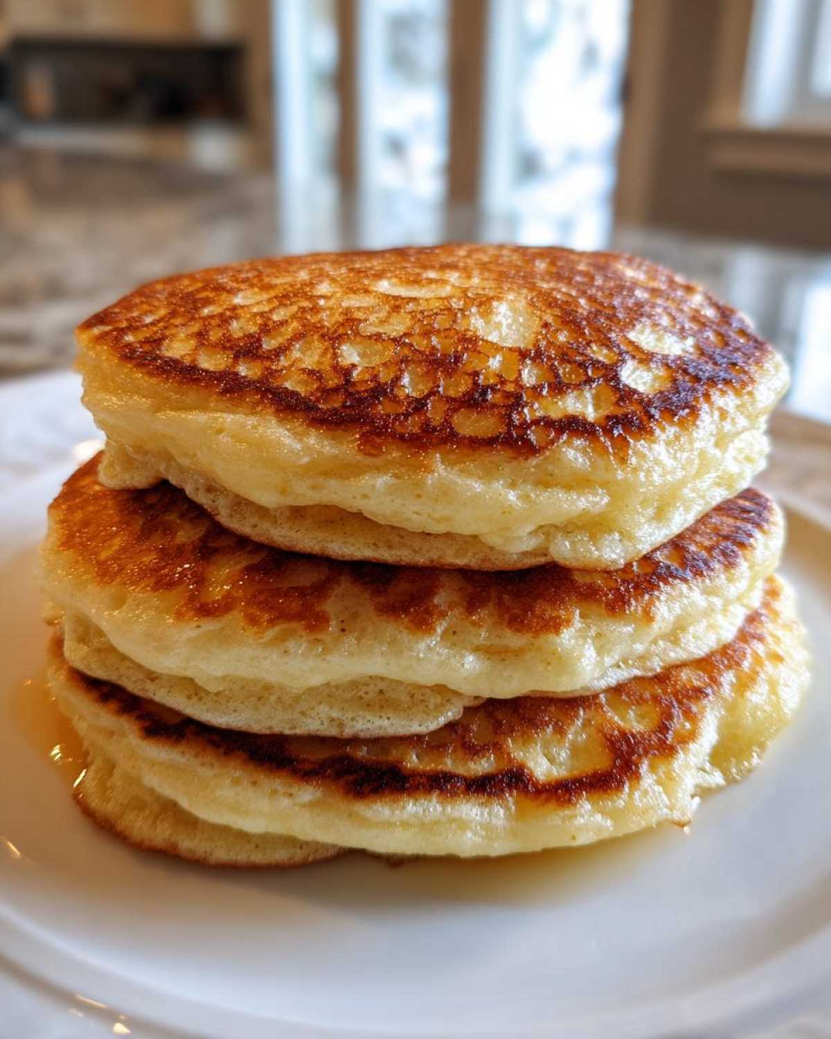 A tall stack of three golden brown, thick, and fluffy pancakes served on a white plate.