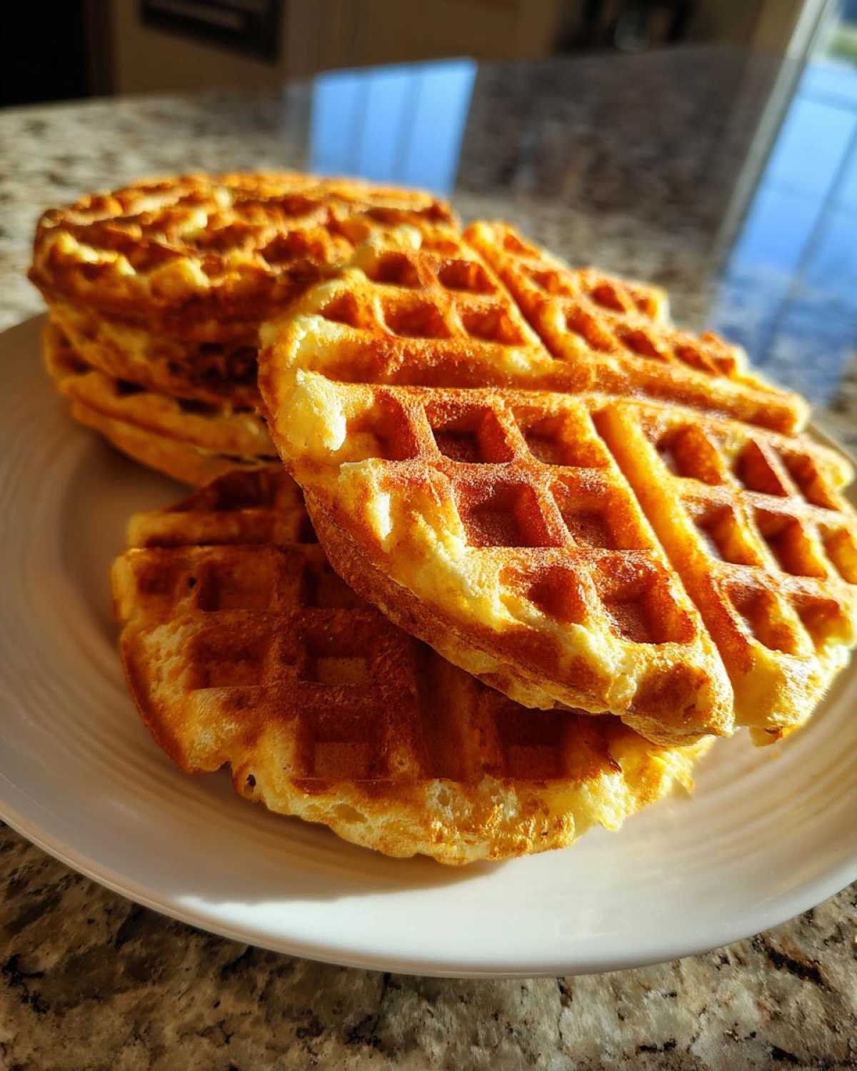 A stack of golden brown, freshly made high protein waffles resting on a white plate.