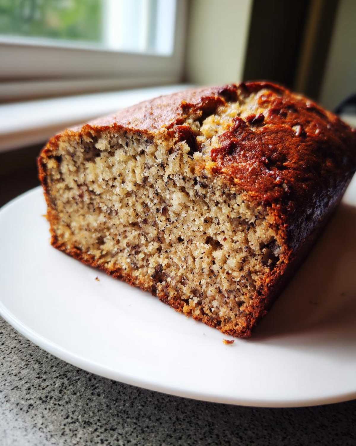 A close-up of a freshly baked slice of sugar free banana bread sitting on a white plate.