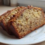 Two thick slices of moist sugar free banana bread topped with pecans resting on a white plate.