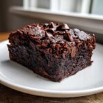Close-up of a rich, dark square of sweet potato brownies topped with melted chocolate chips.