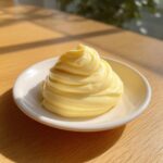 A beautiful swirl of creamy, pale yellow homemade mayonnaise served on a small white dish.