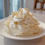 A large, perfectly piped mound of light yellow vanilla buttercream frosting sitting on a white plate.