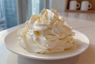 A large, perfectly piped mound of light yellow vanilla buttercream frosting sitting on a white plate.