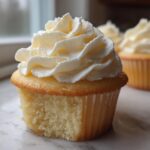 A close-up shot showing the moist crumb and generous swirl of frosting on one of the amazing vanilla cupcakes.