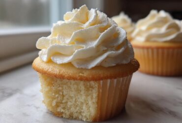 A close-up shot showing the moist crumb and generous swirl of frosting on one of the amazing vanilla cupcakes.