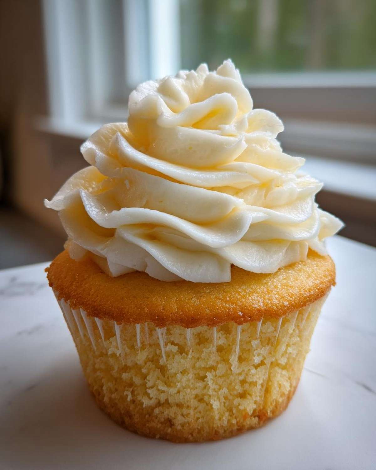 A close-up of a single, perfectly baked vanilla cupcake topped with a tall swirl of creamy white vanilla frosting.