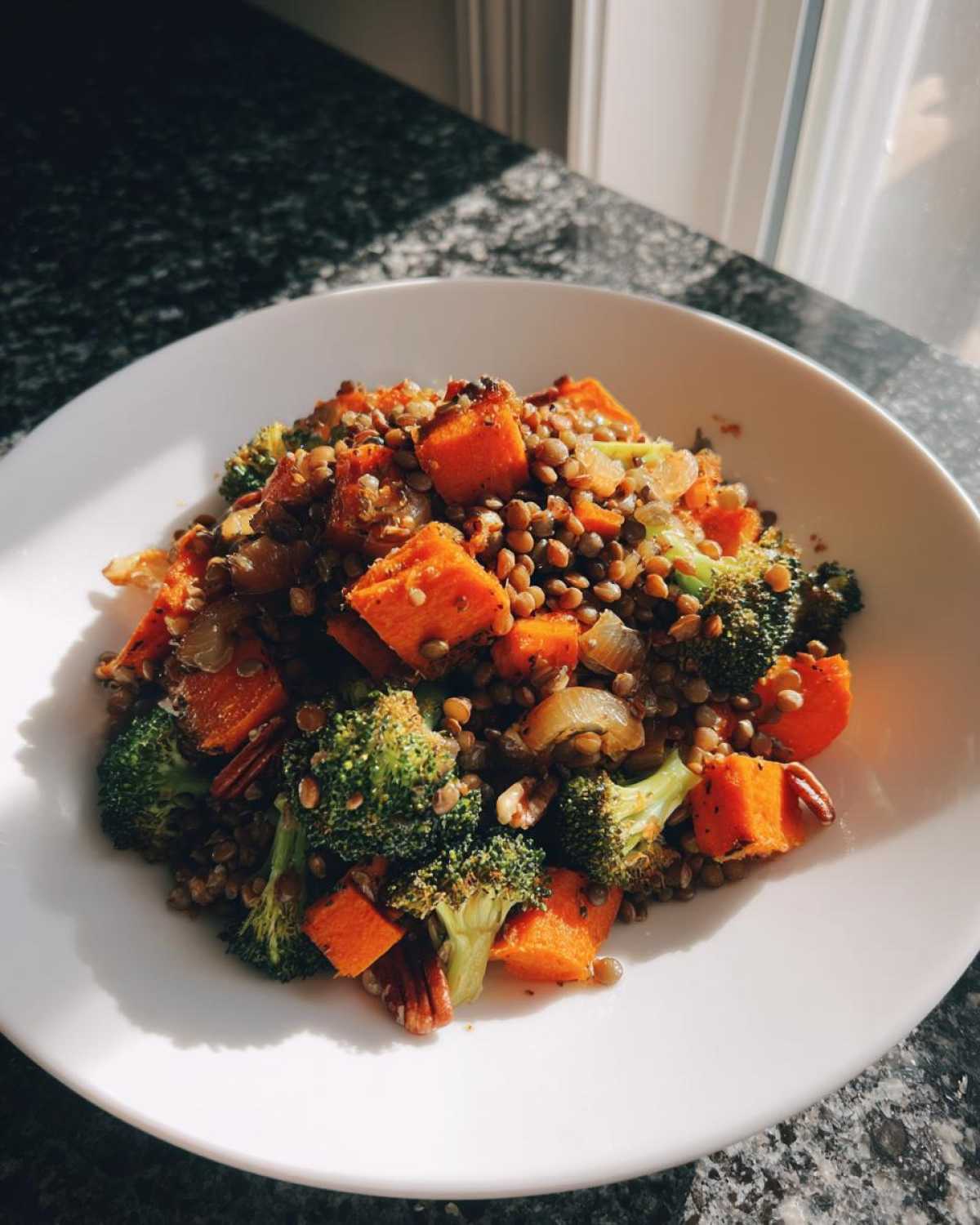 A bright, sunlit bowl of veggie lentil salad featuring lentils, roasted sweet potato cubes, and broccoli florets.