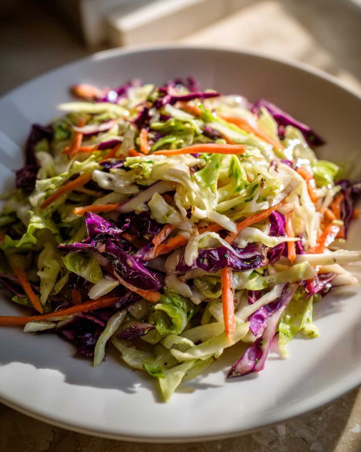 A close-up of a fresh, colorful cabbage salad featuring shredded green and red cabbage and carrots.