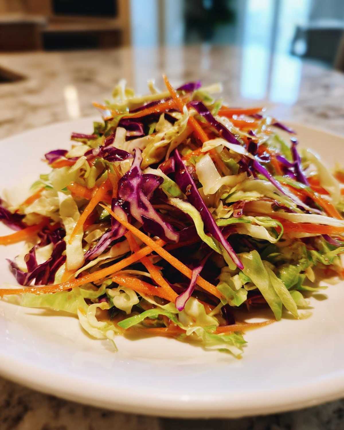 A close-up of a vibrant, freshly dressed cabbage salad featuring shredded green and purple cabbage and bright orange carrots.