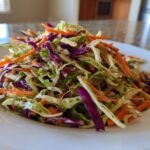 Close-up of a vibrant, freshly dressed cabbage salad featuring shredded green cabbage, purple cabbage, and bright orange carrots.