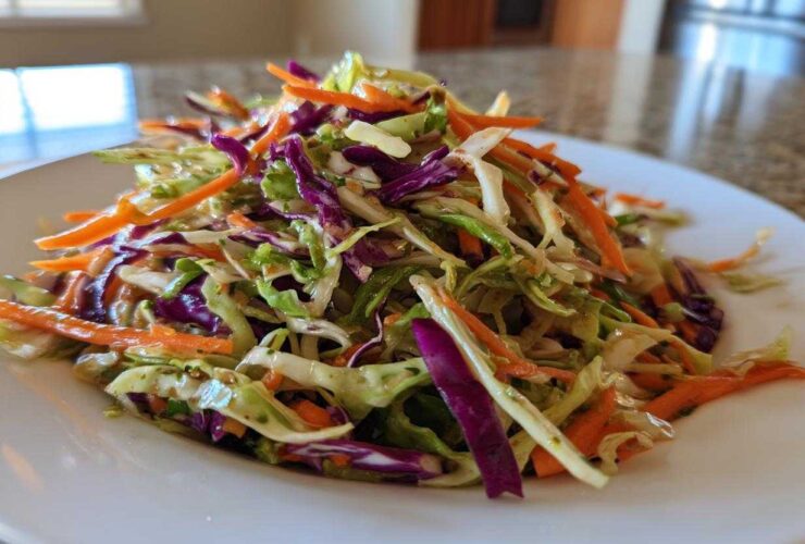 Close-up of a vibrant, freshly dressed cabbage salad featuring shredded green cabbage, purple cabbage, and bright orange carrots.