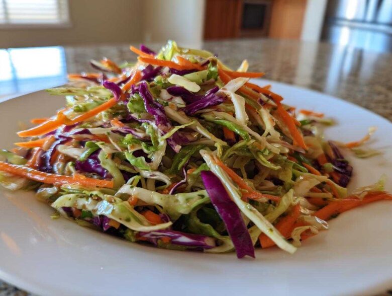 Close-up of a vibrant, freshly dressed cabbage salad featuring shredded green cabbage, purple cabbage, and bright orange carrots.