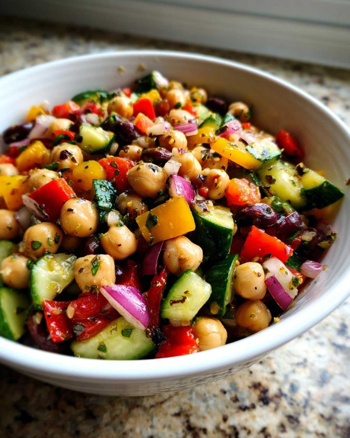 Close-up of a vibrant, fresh bean salad featuring chickpeas, cucumbers, red onion, and bell peppers.