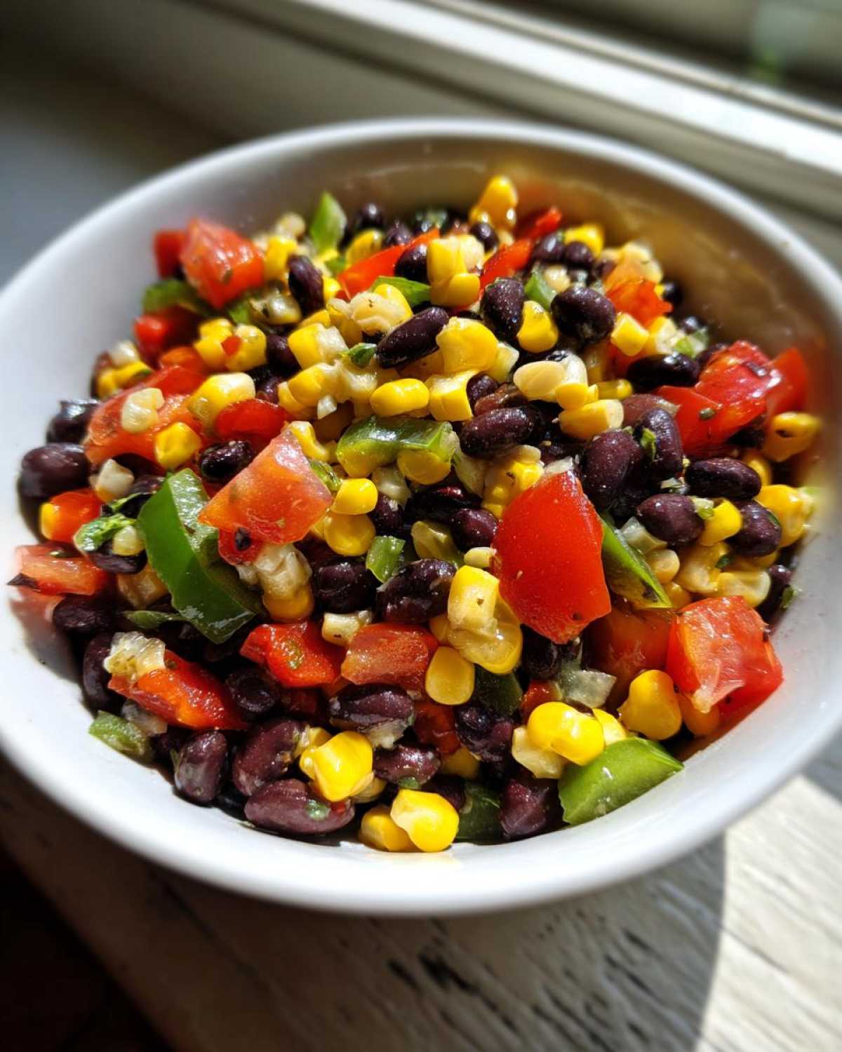 Close-up of fresh cowboy caviar featuring black beans, corn, tomatoes, and green peppers in a white bowl.