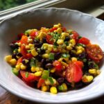 Close-up of a white bowl filled with colorful cowboy caviar featuring corn, black beans, tomatoes, and peppers.