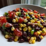 Close-up of a white bowl filled with colorful cowboy caviar featuring black beans, corn, tomatoes, and peppers.