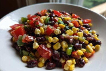Close-up of a white bowl filled with colorful cowboy caviar featuring black beans, corn, tomatoes, and peppers.