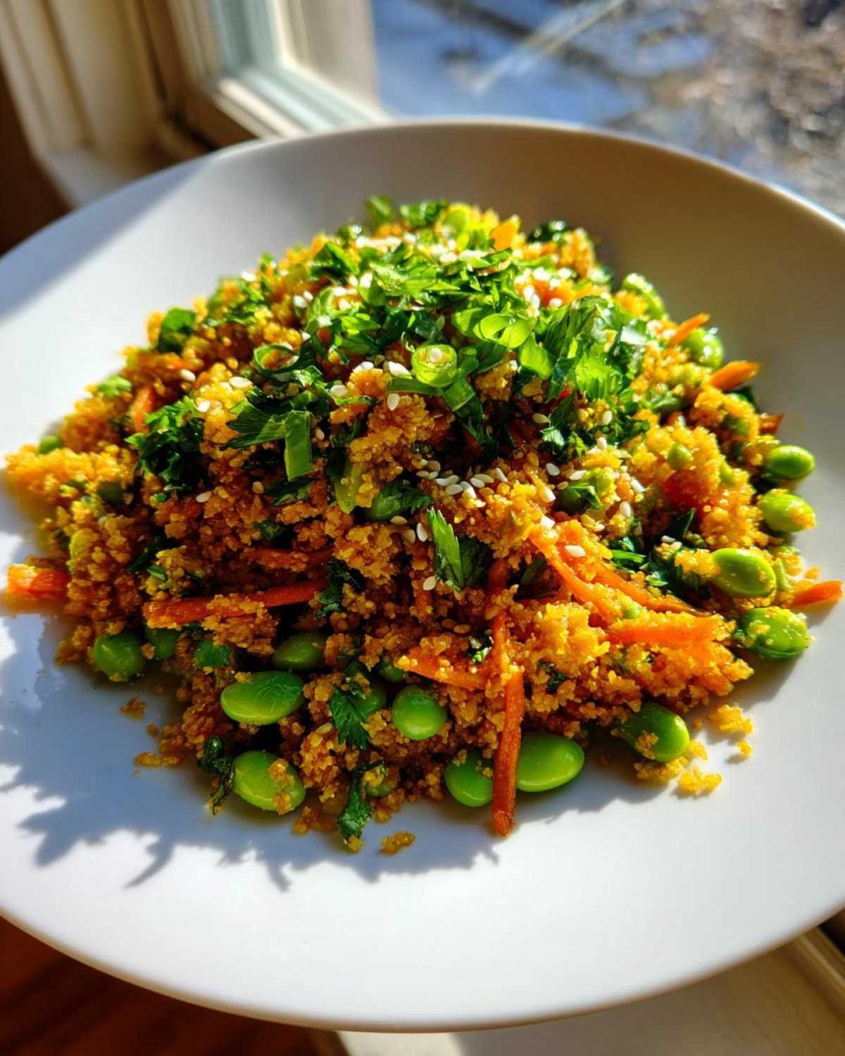 A close-up of a serving of vibrant, seasoned crispy rice salad mixed with bright green edamame and shredded carrots, topped with fresh herbs.
