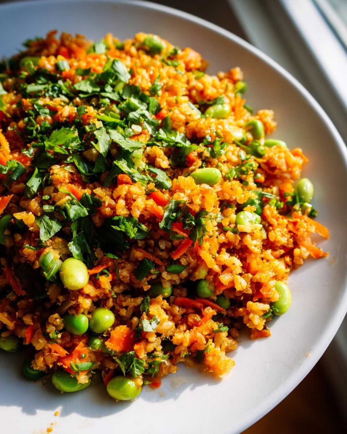 Close-up of a vibrant, orange-hued crispy rice salad mixed with bright green edamame and topped with fresh parsley.