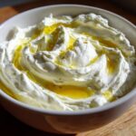 Close-up of creamy, bright white whipped feta dip topped generously with golden olive oil.