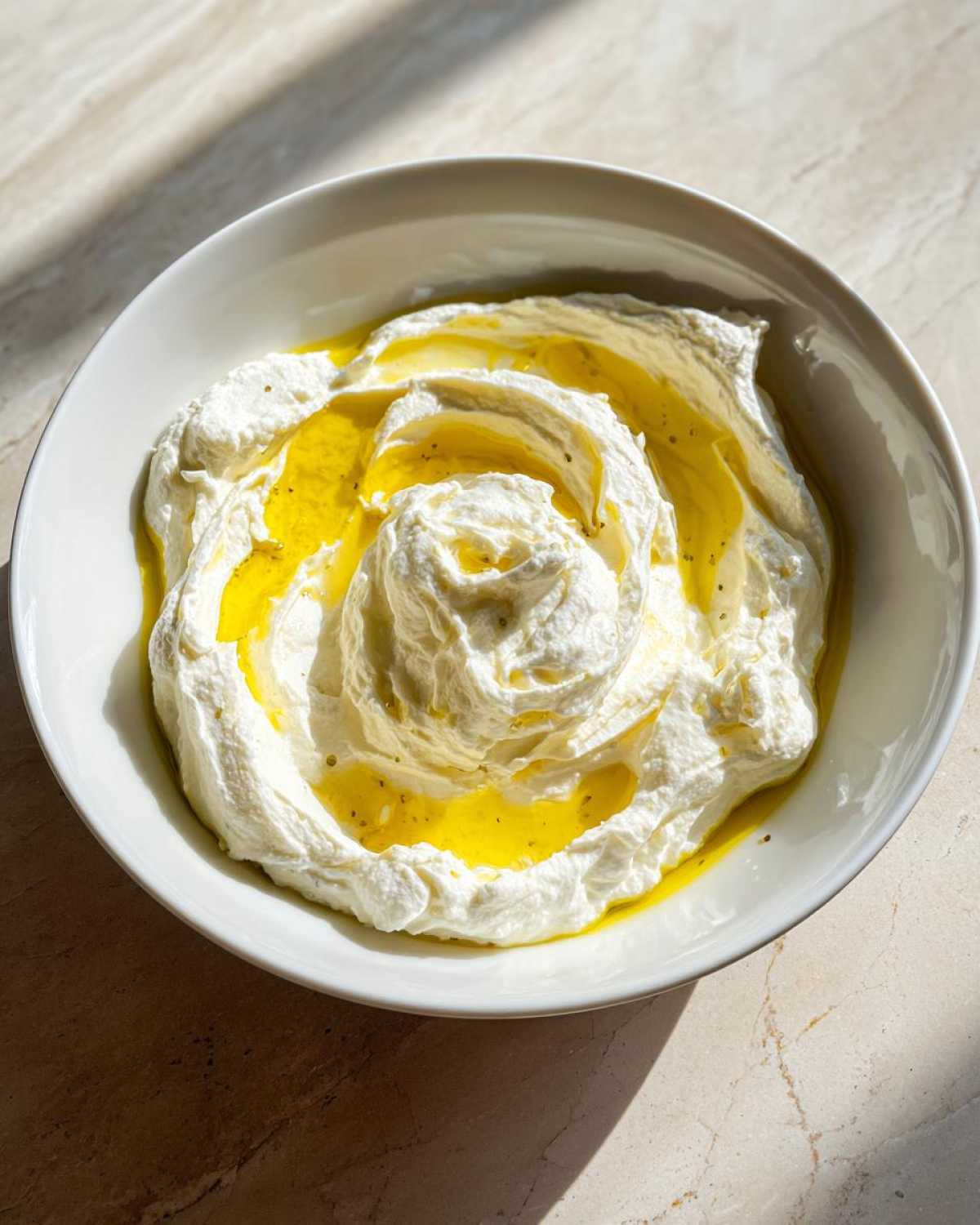 A white bowl filled with creamy whipped feta dip, swirled and topped with bright yellow olive oil.