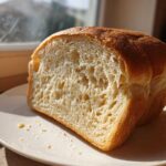 Two thick slices of freshly baked whole wheat bread showing a soft, airy crumb texture on a white plate.