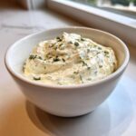 A close-up of thick, creamy 5-Minute Greek Yogurt Ranch Dip topped with fresh chopped herbs in a white bowl.