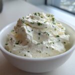 A white bowl filled with fluffy 5-Minute Greek Yogurt Ranch Dip, topped with fresh chopped chives.