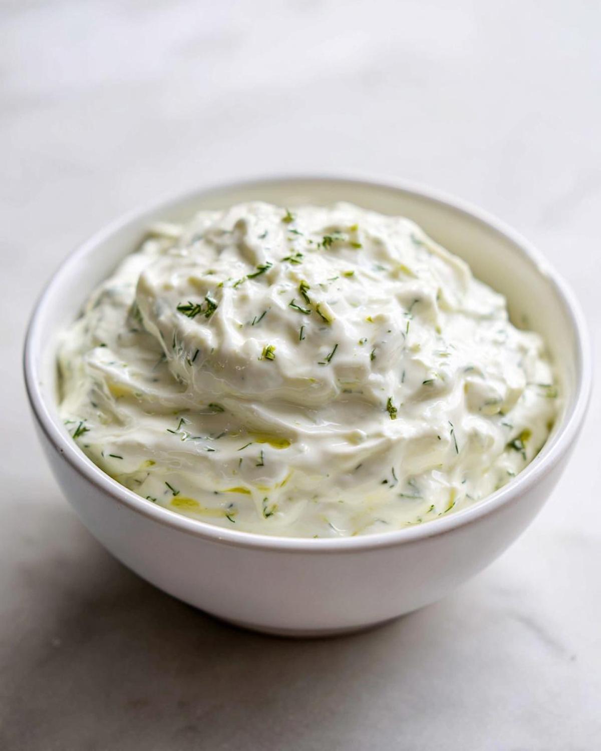 Close-up of creamy 5-Minute Greek Yogurt Ranch Dip topped with fresh green herbs in a white bowl.
