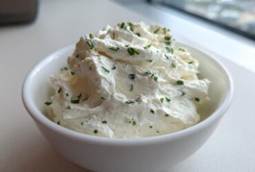 A white bowl filled with fluffy 5-Minute Greek Yogurt Ranch Dip, topped with fresh chopped chives.