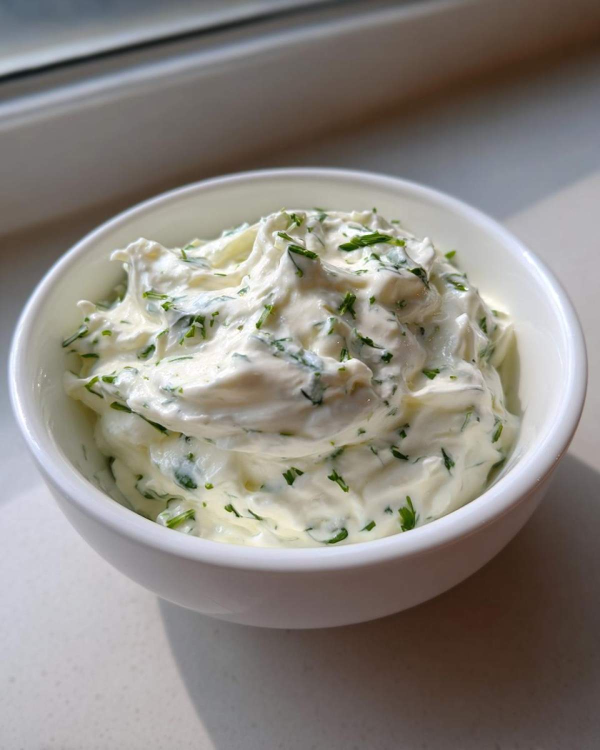 A close-up of thick, creamy 5-Minute Greek Yogurt Ranch Dip speckled with fresh green herbs in a small white bowl.