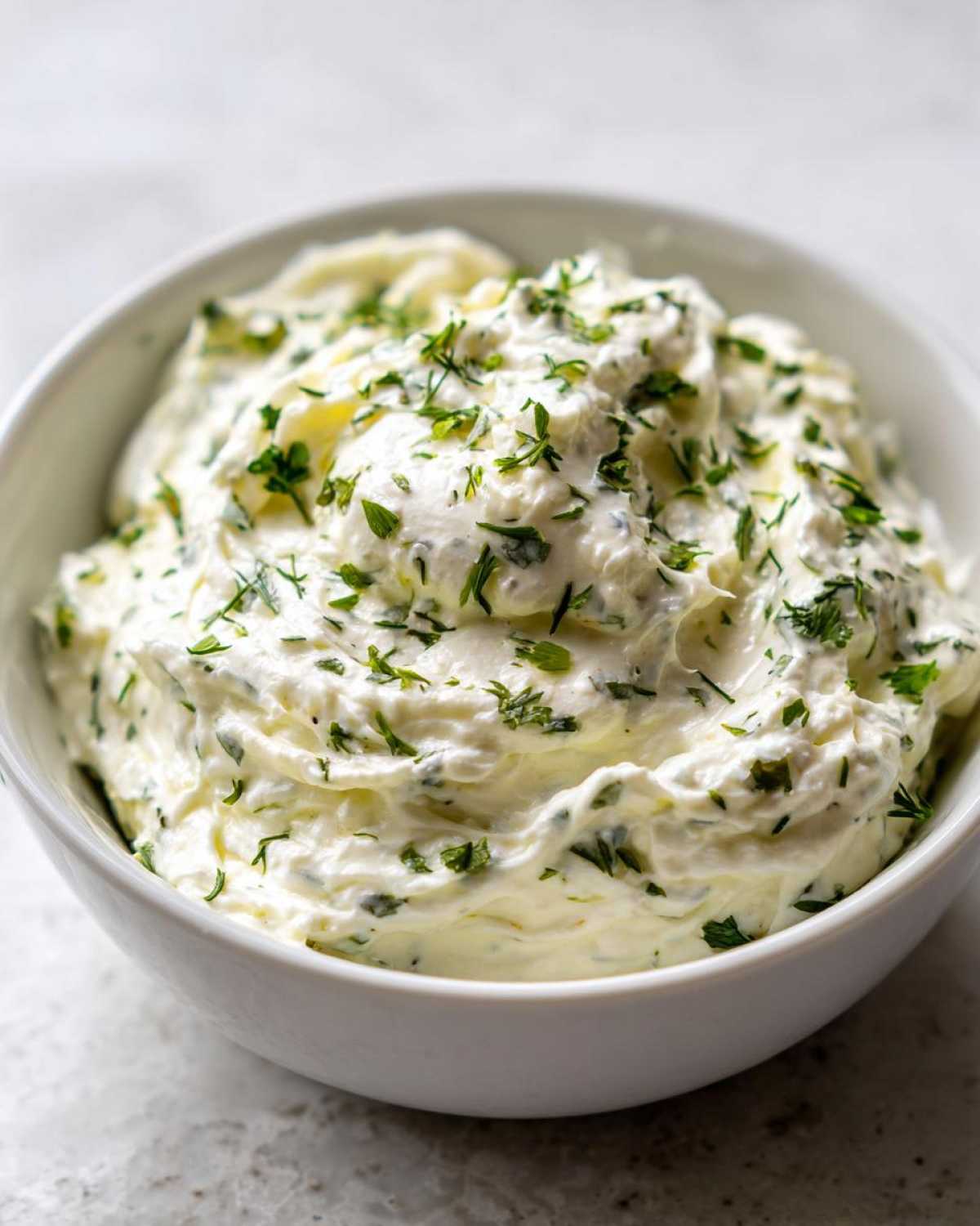 Close-up of thick, creamy 5-Minute Greek Yogurt Ranch Dip topped generously with fresh green herbs.