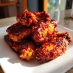 A pile of glossy, saucy Air Fryer BBQ Chicken Wings stacked high on a white plate, glistening under sunlight.