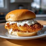 Close-up of an Air Fryer Crispy Fish Sandwich with Tartar Sauce on a brioche bun, served on a white plate.