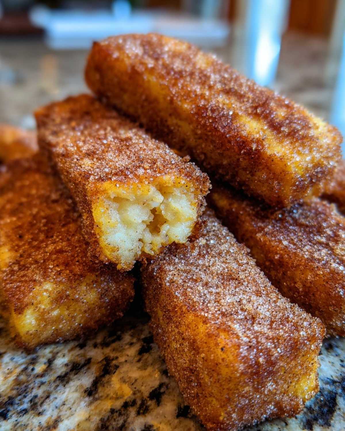 Close-up of golden Air Fryer French Toast Sticks heavily coated in cinnamon sugar, one stick is broken open.