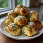 A stack of golden brown Air Fryer Garlic Knots topped with melted butter, parsley, and grated Parmesan cheese.