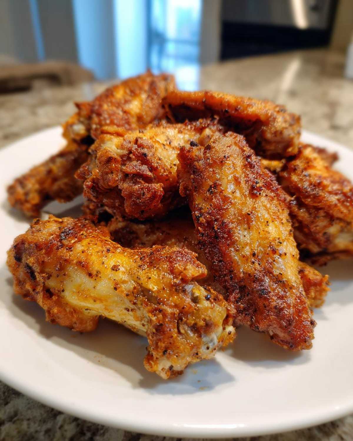 A pile of perfectly cooked, crispy Air Fryer Lemon Pepper Wings seasoned with visible black pepper flakes, served on a white plate.