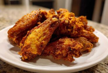 A close-up of crispy, golden-brown Air Fryer Lemon Pepper Wings piled high on a white plate.