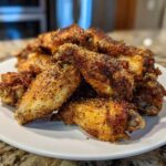A pile of crispy, golden brown Air Fryer Lemon Pepper Wings heavily seasoned with black pepper on a white plate.