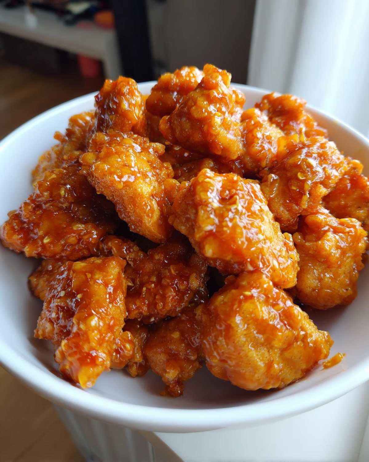Close-up of crispy, glazed pieces of Air Fryer Orange Chicken piled high in a white bowl.