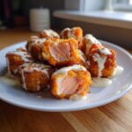 A plate of crispy Air Fryer Salmon Bites drizzled generously with creamy Bang Bang Sauce.