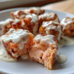 Close-up of flaky Air Fryer Salmon Bites covered in creamy Bang Bang Sauce on a white plate.