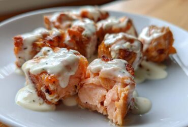 Close-up of flaky Air Fryer Salmon Bites covered in creamy Bang Bang Sauce on a white plate.