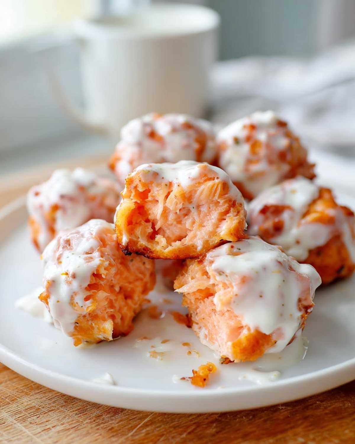 Close-up of flaky Air Fryer Salmon Bites covered in a creamy white sauce, one bite is broken open.