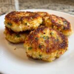 A stack of golden brown, crispy Air Fryer Salmon Patties seasoned with visible green herbs on a white plate.