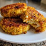 Close-up of three crispy, golden Air Fryer Salmon Patties stacked on a white plate, one is broken open showing the interior.