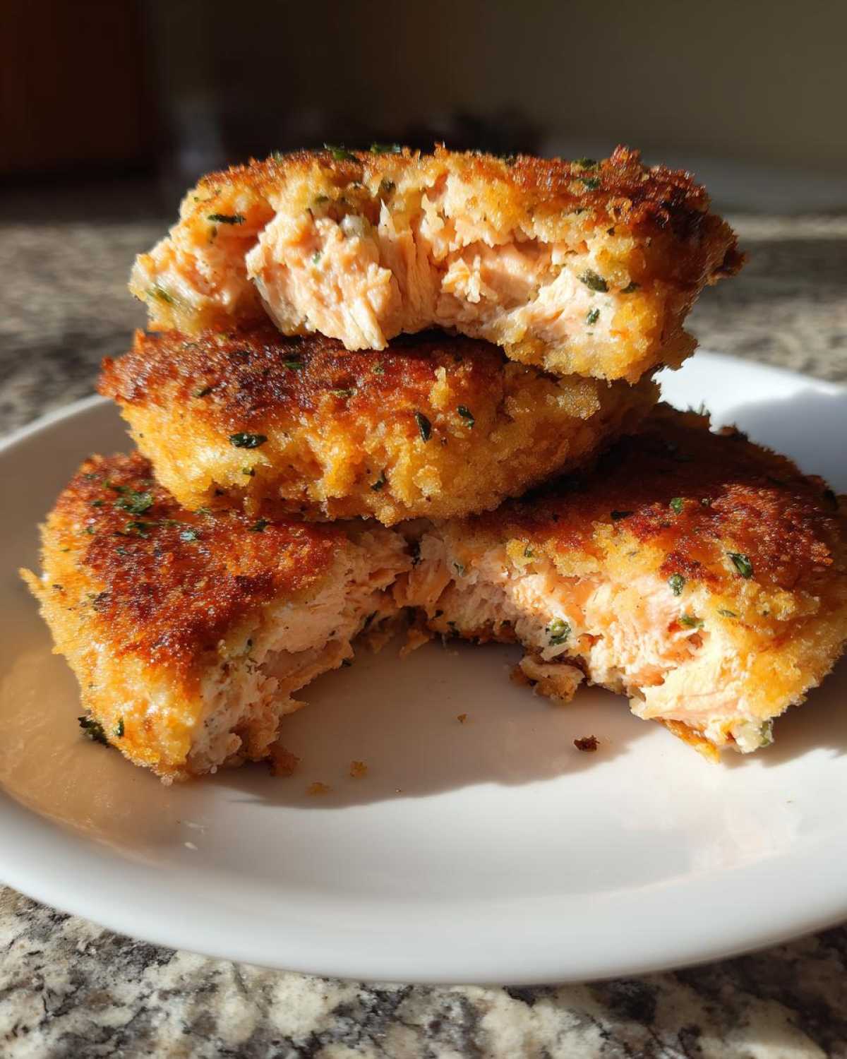 Three golden brown Air Fryer Salmon Patties stacked, with the top and bottom ones broken open to show the flaky pink salmon interior.