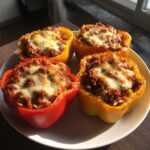Four colorful Air Fryer Stuffed Bell Peppers, filled with meat and rice and topped with melted cheese, served on a white plate.